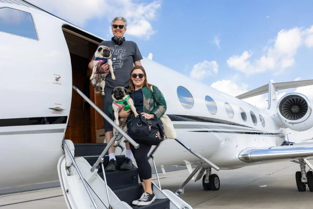 Two travelers holding dogs beside a private jet